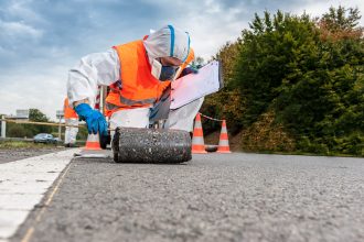 Technicien en tenue SS4 sur chantier routier prélevant une carotte d'enrobé avec risque d'amiante et d'HAP